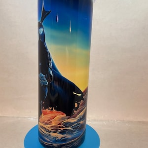K&ouml;nnte beinhalten: Ein zylindrischer Edelstahlbecher mit einem umlaufenden Grafikdruck einer dunklen, umhangtragenden Figur, die auf einer felsigen, w&uuml;stenartigen Landschaft unter einem D&auml;mmerungshimmel steht, der von tiefem Blau zu Orange &uuml;bergeht.