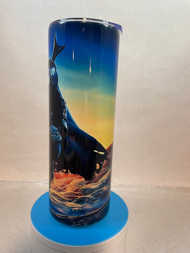 K&ouml;nnte beinhalten: Ein zylindrischer Edelstahlbecher mit einem umlaufenden Grafikdruck einer dunklen, umhangtragenden Figur, die auf einer felsigen, w&uuml;stenartigen Landschaft unter einem D&auml;mmerungshimmel steht, der von tiefem Blau zu Orange &uuml;bergeht.