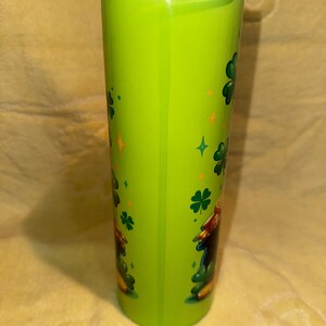 Może przedstawiać: Zielony kubek z czarną pokrywką, ozdobiony koniczyną i złotymi gwiazdami. Kubek ma wz&oacute;r kresk&oacute;wkowego skrzata. Ten izolowany kubek podr&oacute;żny jest idealny do gorących lub zimnych napoj&oacute;w.