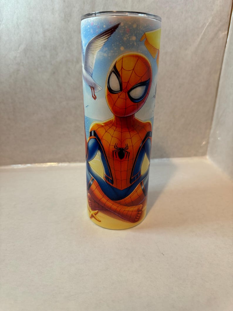 May include: A stainless steel tumbler with a colorful image of Spider-Man on a beach with seagulls flying overhead. The tumbler has a yellow, blue, and red design.