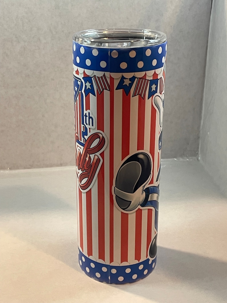 Peut inclure: Un gobelet isotherme rouge, blanc et bleu avec un personnage de dessin anim&eacute; et le texte "4th of July" dessus.