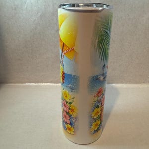 May include: A white stainless steel tumbler with a beach scene design. The design features a yellow umbrella, a blue ocean, a palm tree, and flowers.