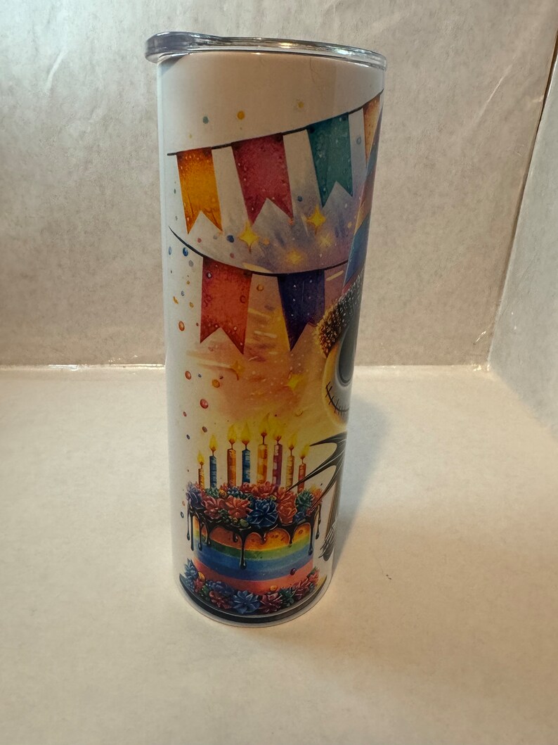 Może przedstawiać: Biały kubek ze stali nierdzewnej z kolorowym wzorem tortu urodzinowego i dekoracji imprezowych. Tort ma tęczowe warstwy, czarny lukier i zapalone świeczki. Wz&oacute;r zawiera r&oacute;wnież kolorowe flagi i gwiazdki.