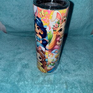May include: A stainless steel tumbler with a black lid, decorated with cartoon characters in Easter bunny costumes. The wrap-around design features princesses and Easter-themed graphics. The background is a light blue.