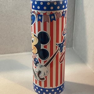 Peut inclure: Un gobelet isotherme rouge, blanc et bleu avec un motif Mickey Mouse. Le gobelet pr&eacute;sente un fond ray&eacute; rouge et blanc avec des pois bleus en haut et en bas. Mickey Mouse tient un parapluie rouge, blanc et bleu et porte un chapeau rouge, blanc et bleu.