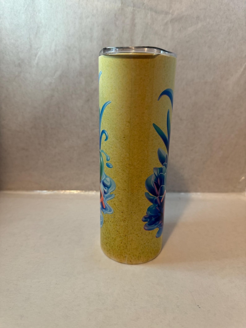 K&ouml;nnte beinhalten: Ein gelber Becher mit einem floralen Design in Blau und T&uuml;rkis. Der Edelstahlbecher hat einen Deckel und eine strukturierte Oberfl&auml;che. Das florale Design befindet sich auf der Vorderseite des Bechers.