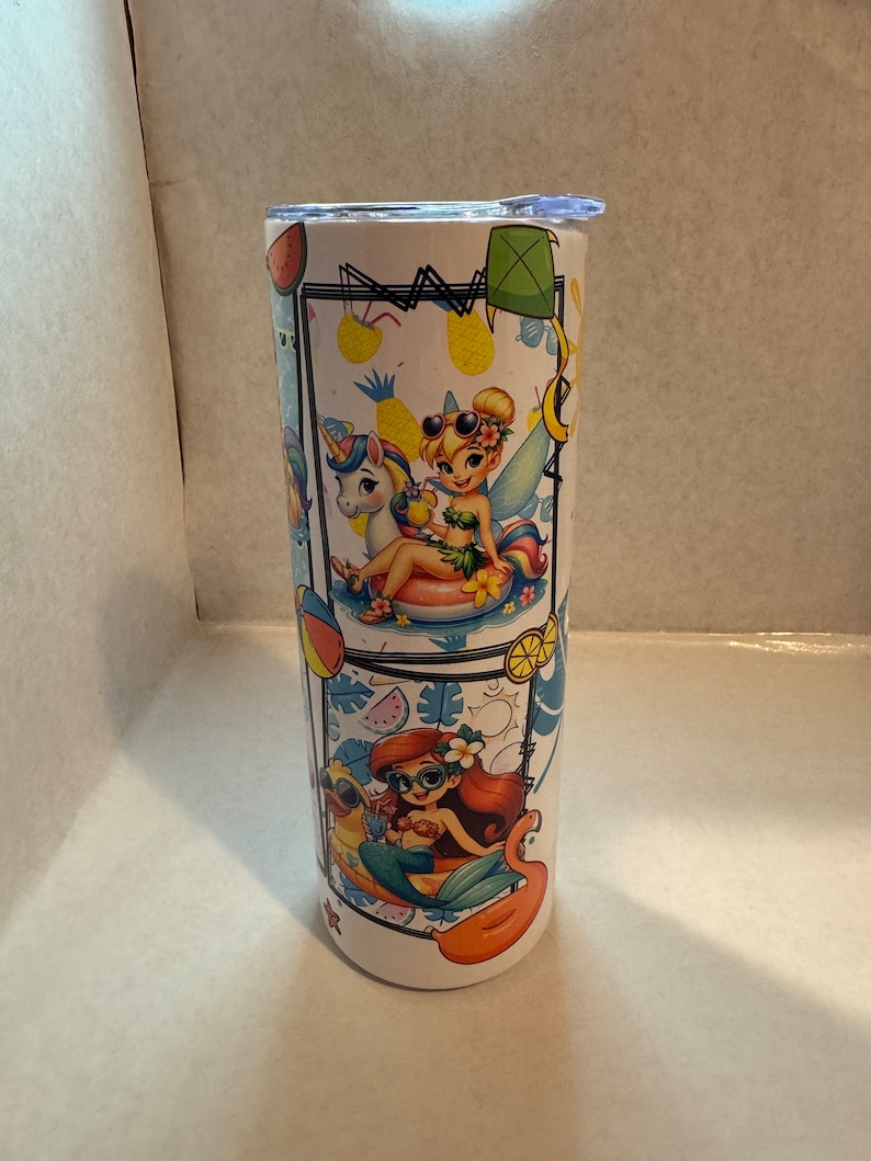 May include: A white stainless steel tumbler with a colourful design featuring cartoon characters. The design includes a mermaid, a fairy, and a unicorn. The characters are all wearing sunglasses and enjoying the summer.