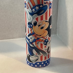 Peut inclure: Un gobelet en acier inoxydable avec un motif patriotique repr&eacute;sentant Mickey Mouse habill&eacute; en Oncle Sam. Le gobelet a une base bleue avec des pois blancs et un motif ray&eacute; rouge, blanc et bleu avec des &eacute;toiles.