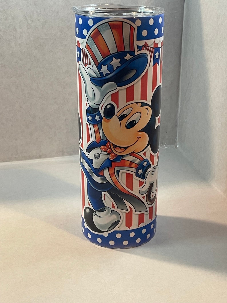 Peut inclure: Un gobelet en acier inoxydable avec un motif patriotique repr&eacute;sentant Mickey Mouse habill&eacute; en Oncle Sam. Le gobelet a une base bleue avec des pois blancs et un motif ray&eacute; rouge, blanc et bleu avec des &eacute;toiles.