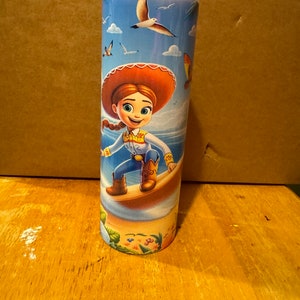 May include: A stainless steel tumbler with a colorful design featuring a cartoon character riding a surfboard. The character is wearing a red hat and blue jeans. The background is a blue sky with white clouds and seagulls.