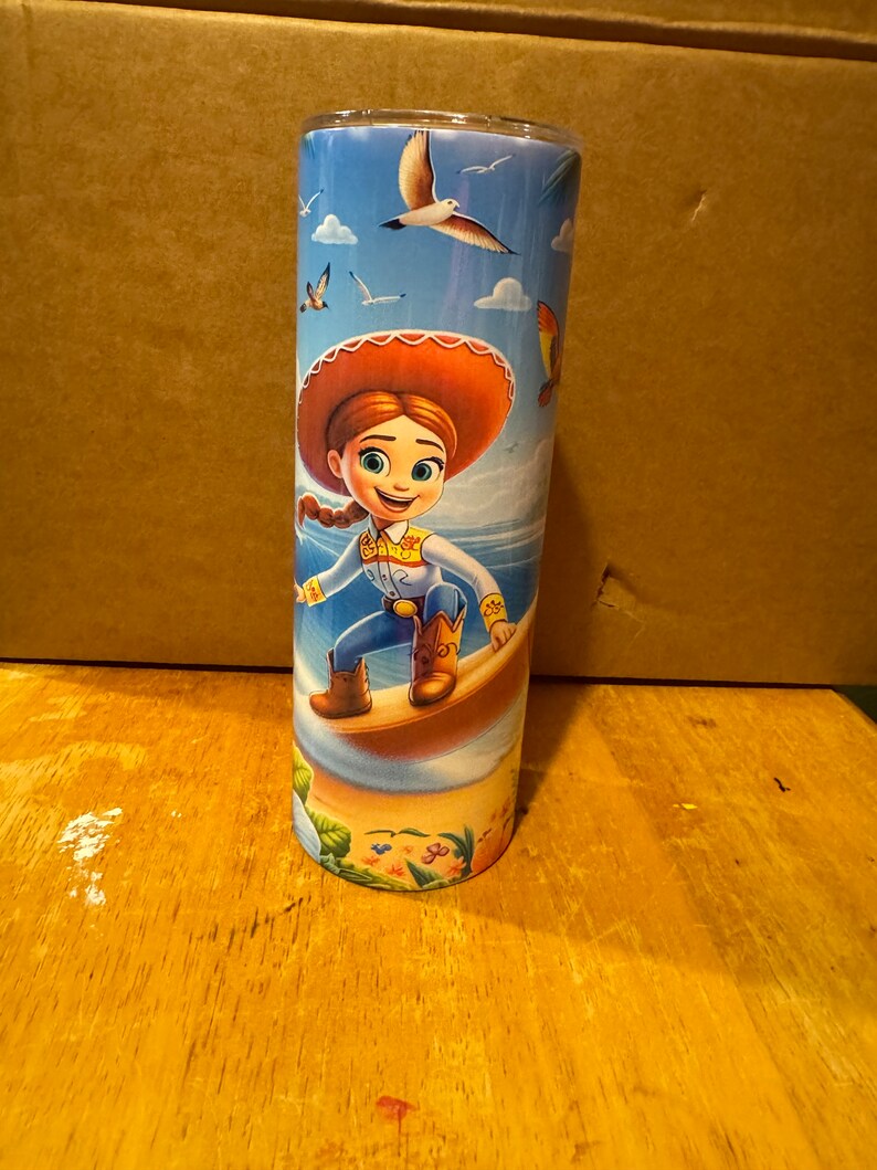 May include: A stainless steel tumbler with a colorful design featuring a cartoon character riding a surfboard. The character is wearing a red hat and blue jeans. The background is a blue sky with white clouds and seagulls.