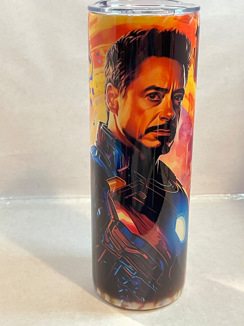 May include: A stainless steel tumbler with a colorful image of Iron Man from the Marvel Cinematic Universe. The image features Iron Man's face and a close-up of his suit.