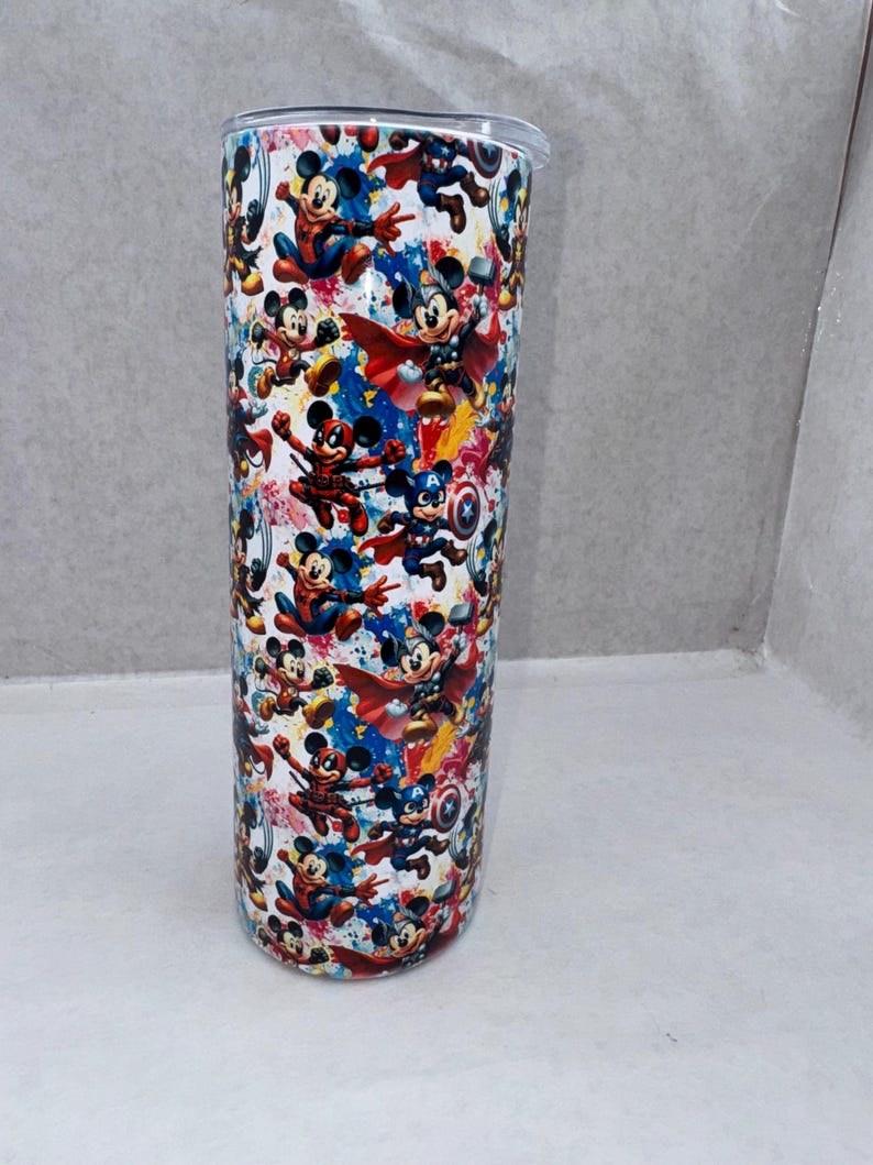 May include: A cylindrical stainless steel tumbler featuring a repeating pattern of Mickey Mouse dressed as various superheroes, including Captain America, Thor, and Spider-Man, set against a vibrant, multi-colored paint splatter background.