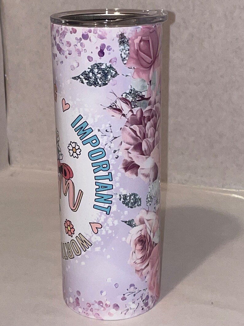 May include: A stainless steel tumbler with a floral design and the text "Important Work" in pink and blue lettering. The tumbler has a white background with a pink and purple floral pattern.