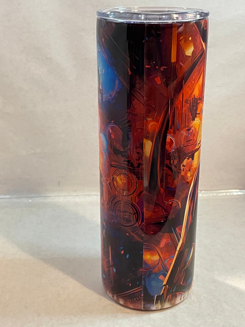 May include: A stainless steel tumbler with a colorful abstract design featuring shades of orange, blue, and yellow. The design appears to be a close-up of a complex machine or engine.