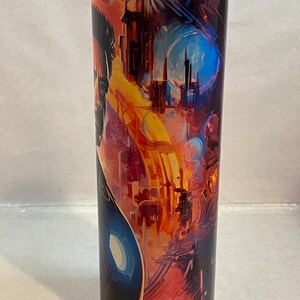 May include: A stainless steel tumbler with a colorful abstract design featuring a superhero character. The design includes a cityscape, a blue sky, and a yellow and orange sunset.