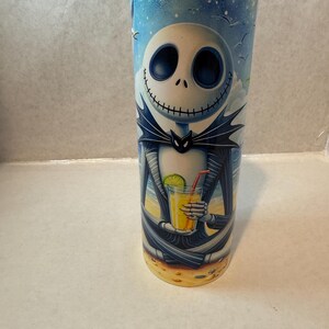 May include: A stainless steel tumbler with a colorful image of Jack Skellington from The Nightmare Before Christmas, holding a tropical drink on a beach.