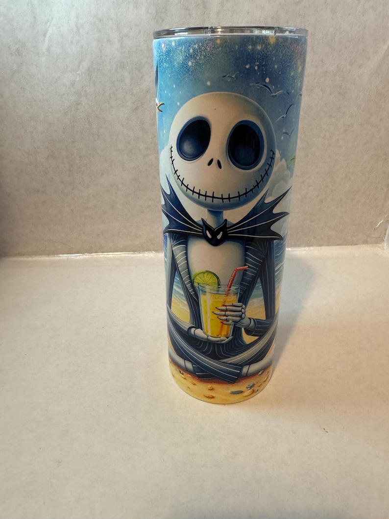 May include: A stainless steel tumbler with a colorful image of Jack Skellington from The Nightmare Before Christmas, holding a tropical drink on a beach.