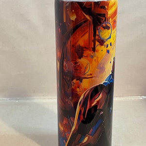 May include: A stainless steel tumbler with a colorful abstract design featuring a spaceship in a galaxy. The tumbler has a clear lid.