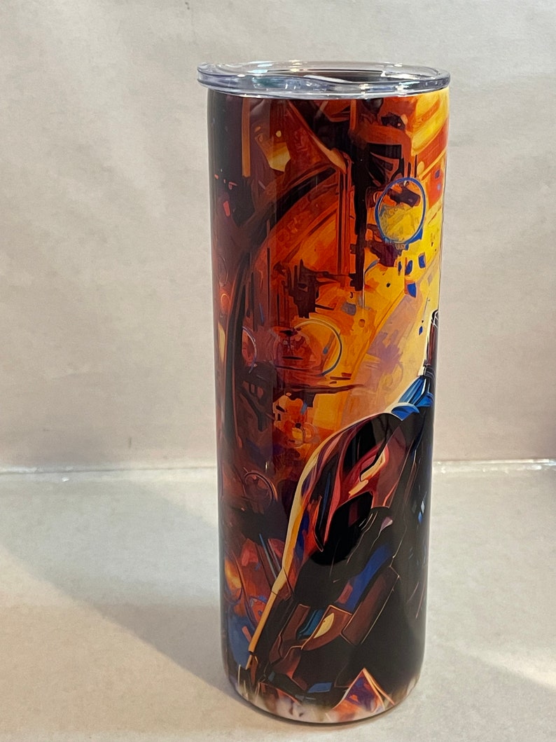 May include: A stainless steel tumbler with a colorful abstract design featuring a spaceship in a galaxy. The tumbler has a clear lid.