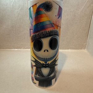 Może przedstawiać: Biały kubek ze stali nierdzewnej z postacią w kolorowym, tęczowym kapeluszu imprezowym. Postać jest ubrana w czarno-biały pasiasty garnitur z czarną muszką. Postać ma zszyte usta, a tło to kolorowa scena imprezowa z konfetti i serpentynami.