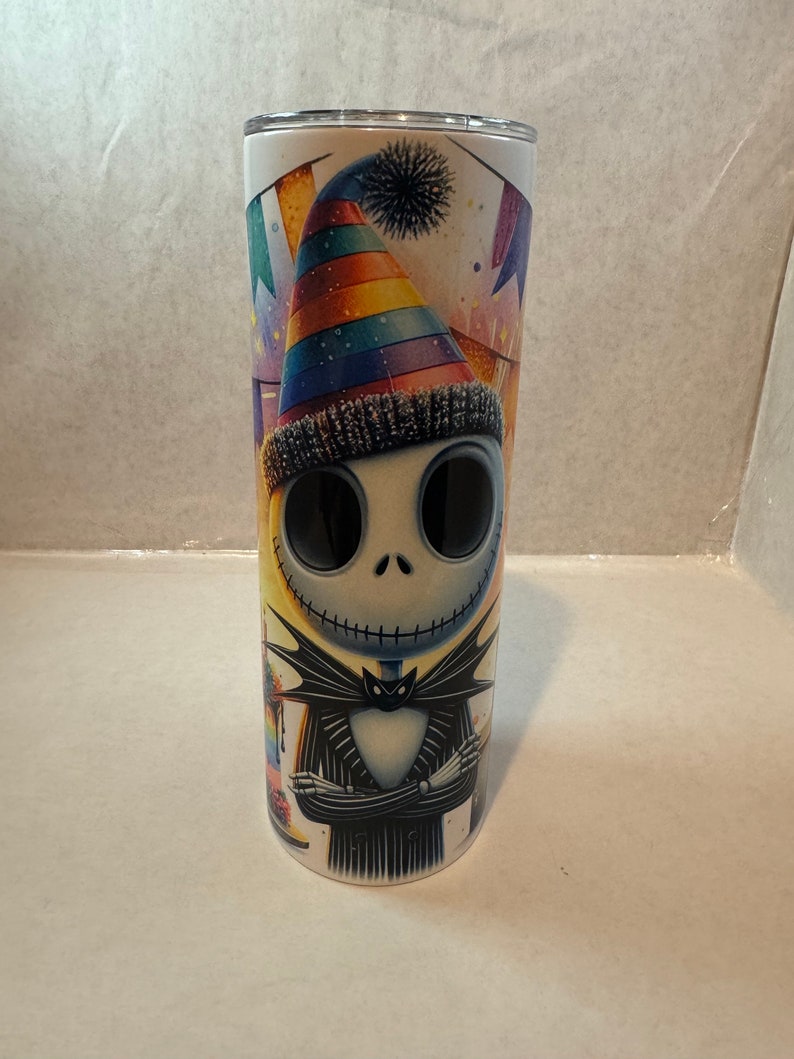 Może przedstawiać: Biały kubek ze stali nierdzewnej z postacią w kolorowym, tęczowym kapeluszu imprezowym. Postać jest ubrana w czarno-biały pasiasty garnitur z czarną muszką. Postać ma zszyte usta, a tło to kolorowa scena imprezowa z konfetti i serpentynami.