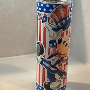 Peut inclure: Un gobelet en acier inoxydable avec un motif patriotique repr&eacute;sentant Mickey Mouse habill&eacute; en Oncle Sam. Le gobelet a un fond ray&eacute; rouge, blanc et bleu avec des pois blancs en haut et en bas.
