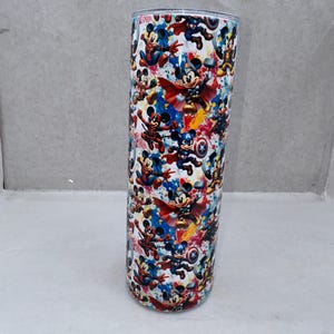 May include: A cylindrical stainless steel tumbler featuring a colorful all-over print of cartoon mice dressed as various superheroes. The design includes characters with capes, shields, and hammers against a vibrant, splattered paint background.
