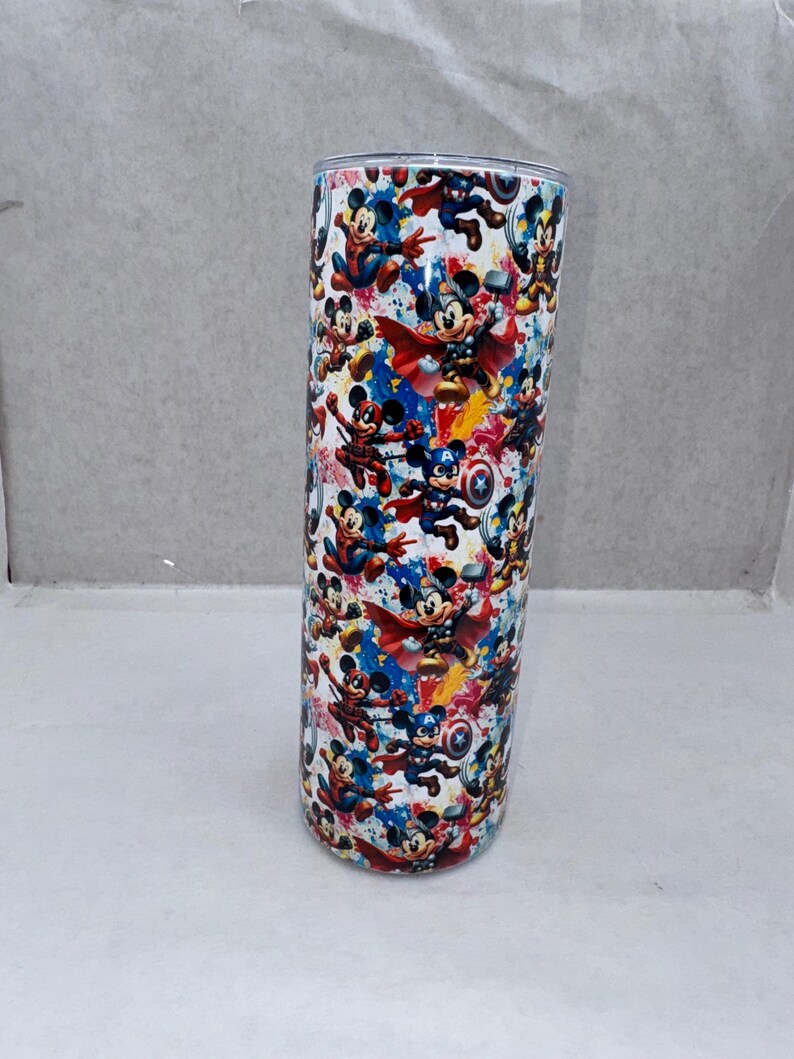May include: A cylindrical stainless steel tumbler featuring a colorful all-over print of cartoon mice dressed as various superheroes. The design includes characters with capes, shields, and hammers against a vibrant, splattered paint background.