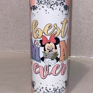 Puede incluir: Un vaso blanco con un fondo moteado en blanco y negro. El vaso tiene un gr&aacute;fico rosa, amarillo y morado que dice "best mom ever" con una imagen de dibujos animados de Minnie Mouse sosteniendo un ramo de flores.