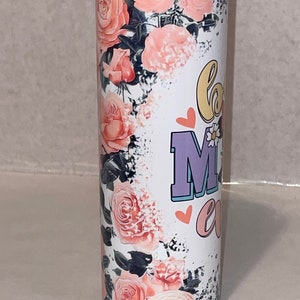 Puede incluir: Un vaso de acero inoxidable blanco con un dise&ntilde;o floral y el texto "Love Mom" en rosa, morado y amarillo. El vaso tiene una tapa negra.