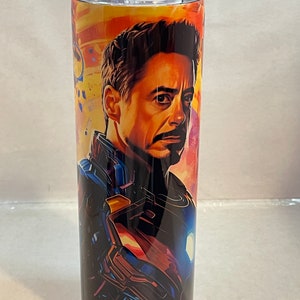 May include: A stainless steel tumbler with a colorful image of Iron Man in his suit. The background is a mix of orange, yellow, and blue.
