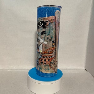 May include: A blue and white glitter tumbler with a pirate map design. The map features a pirate ship, a skull and crossbones, and a treasure chest.