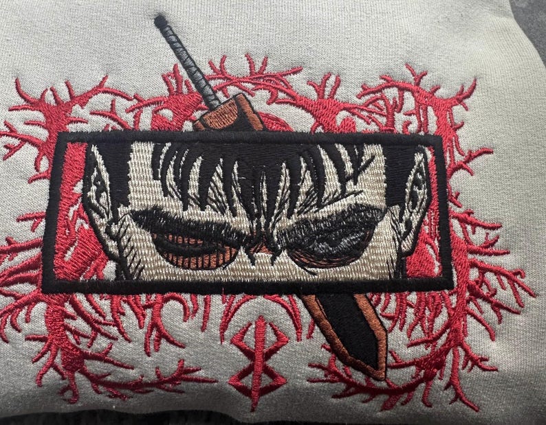 May include: Embroidered patch featuring a close-up of a character's face with a sword behind it. The character has black hair and a serious expression. The background is a red, branching design.