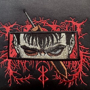 May include: Black embroidered patch with a red and white design. The patch features a close-up of a character's face with a sword behind it. The character has black hair and a serious expression. The sword is partially obscured by the character's face. The patch is surrounded by a red and white design that resembles thorns.
