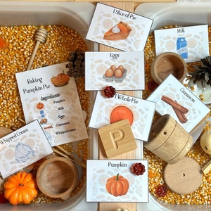 Puede incluir: Un contenedor sensorial lleno de granos de maíz, cuencos de madera, un cubo de madera, un rodillo de madera y una letra P de madera. También hay tarjetas con imágenes y texto, incluyendo "Baking Pumpkin Pie", "Ingredients", "Pumpkin", "Milk", "Eggs", "Cinnamon", "Whipped cream", "1 Slice of Pie", "1 Whole Pie" y "Pumpkin".