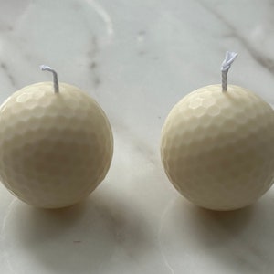 Peut inclure: Deux bougies blanches en forme de balle de golf avec des mèches blanches.
