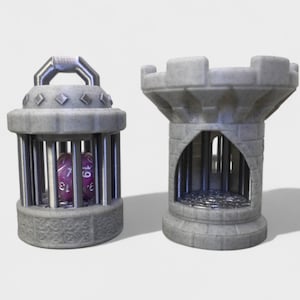 Puede incluir: Dos soportes para dados grises impresos en 3D. Uno es una jaula con asa, que contiene un dado morado. El otro es una torre con un arco abierto. Ambos están diseñados para parecerse a estructuras medievales en miniatura.
