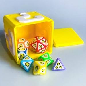 May include: A yellow cube with a white number 3 on top, open to reveal colourful polyhedral dice. The dice are various shapes and colours, including red, blue, green, yellow, and purple, each with a number.