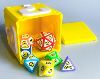 May include: A bright yellow cube with a white number 3 on top, open to reveal colorful polyhedral dice. The dice are various shapes and colors, including red, blue, green, yellow, and purple, each with a number.