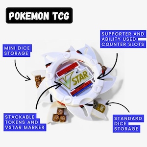 Peut inclure: Accessoire de jeu Pokemon TCG blanc et rouge avec un marqueur VSTAR, des rangements pour mini et dés standards, et des jetons empilables. L'accessoire comporte des emplacements pour les compteurs de soutien et de capacité. Le texte "POKEMON TCG" est en haut.