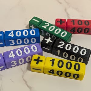 May include: A collection of six multi-colored game dice in blue, green, red, purple, black, and yellow. Each die features printed numbers such as 1000, 2000, 3000, and 4000, along with plus and minus symbols on the smaller square faces.