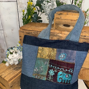 May include: A blue denim tote bag with patchwork details. The patchwork includes a variety of fabrics, including denim, velvet, and sequins. The bag features an embroidered elephant design.