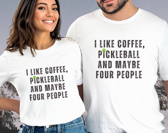 Op de afbeelding: Twee witte T-shirts met een verweerde zwarte afbeelding waarop staat "Ik hou van koffie, pickleball en misschien vier mensen". De afbeelding bevat een groen pickleball-icoon.