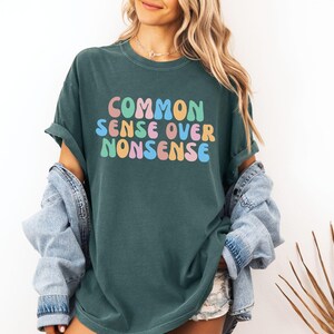 May include: A dark green t-shirt with the text "COMMON SENSE OVER NONSENSE" in colorful, rounded letters.