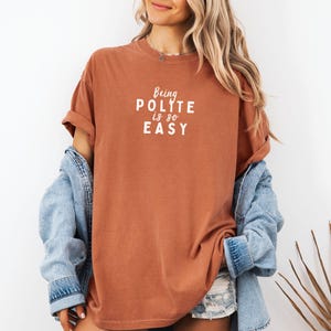 May include: A rust-colored t-shirt with the text "Being Polite is so Easy" in white lettering.