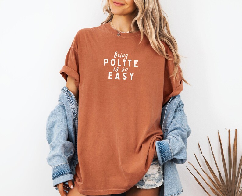 May include: A rust-colored t-shirt with the text "Being Polite is so Easy" in white lettering.