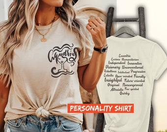 Puede incluir: Una camiseta beige con un gráfico negro de la cara de una mujer con la palabra "Undine" encima. La parte posterior de la camiseta tiene una lista de rasgos de personalidad en texto negro, incluyendo "Excéntrico", "Humanitario curioso", "Independiente", "Innovador", "Visionario", "No convencional", "Rebelde", "Intelectual", "Progresivo", "Ecléctico", "De mente abierta", "Amigable", "Perspicaz", "Orientado al futuro", "Original", "No conformista", "Altruista", "De espíritu libre" y "Excéntrico". El texto "PERSONALITY SHIRT" está impreso debajo de la lista de rasgos.