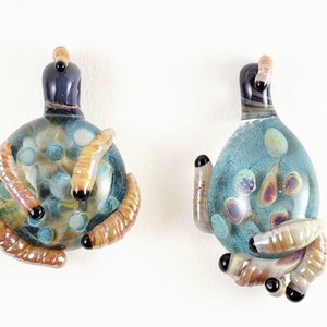 May include: Two glass pendants with a blue and white marbled design. Each pendant is decorated with small brown glass worms.