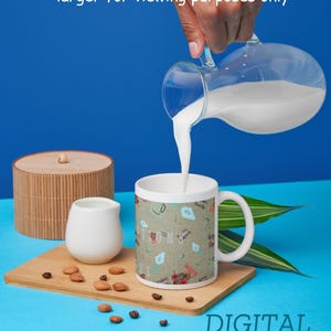 K&ouml;nnte beinhalten: Eine wei&szlig;e Tasse mit Muster wird mit Milch aus einem Glaskrug gef&uuml;llt. Die Tasse steht auf einem Holzbrett mit einem kleinen wei&szlig;en Krug, einem Bambusbeh&auml;lter und verstreuten Mandeln und Kaffeebohnen. Der Text "DIGITAL DOWNLOAD ONLY" ist sichtbar.